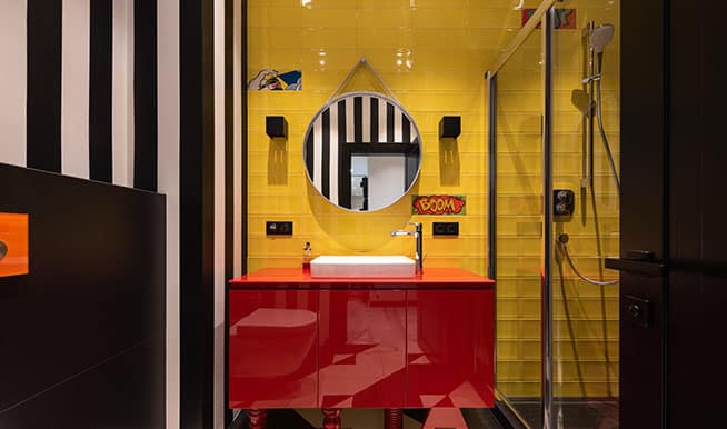 A bold, colorful bathroom with yellowtiles behind the vanity, a red cabinet, and black and white pinstripe wallpaper