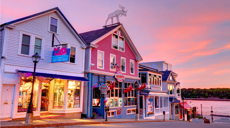 A row of cute New England shops in Bar Harbor, Maine, during sunset. The road leads down to the water.
