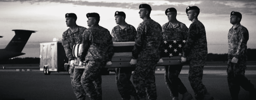 A black-and-white image of military members serving in Mortuary Affairs, carrying a coffin covered by an American flag.