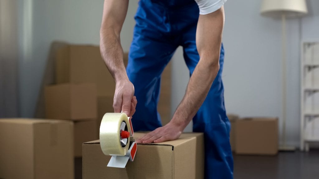 A man in overalls tapes a box shut before his cross-country move