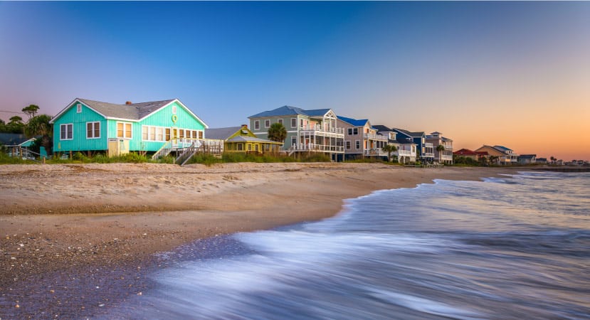 The sun is setting in the distance as waves crawl along the sand in front of large, beachfront homes in Edisto Beach, South Carolina. 