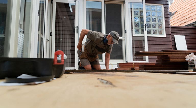 A man nailing down deck boards to extend its length