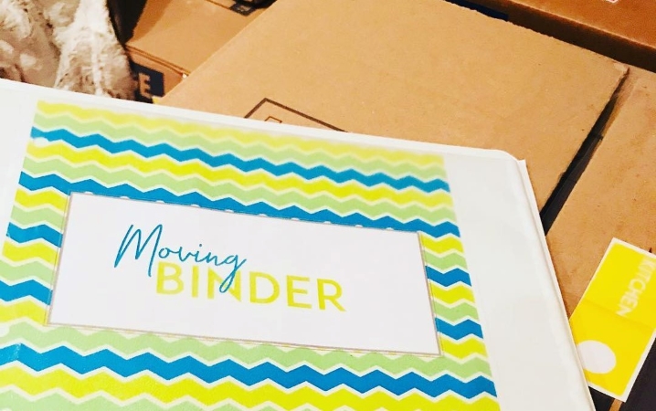 A colorfully decorated moving binder is resting on top of a moving box. The binder is used to keep track of the apartment moving checklist and other important paperwork related to moving.
