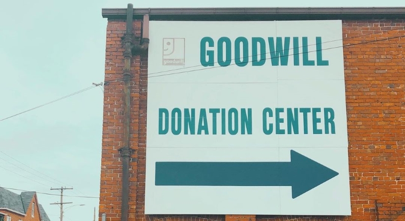 A huge Goodwill Donation Center sign on the side of a brick building. The sign features a giant arrow pointing toward the entrance. 