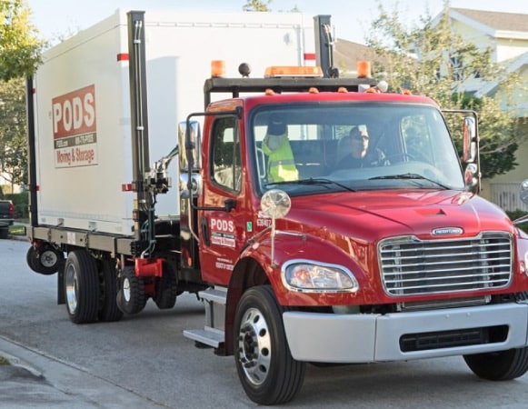 A PODS truck driver is transporting a PODS portable moving container through a residential neighborhood to its final destination.