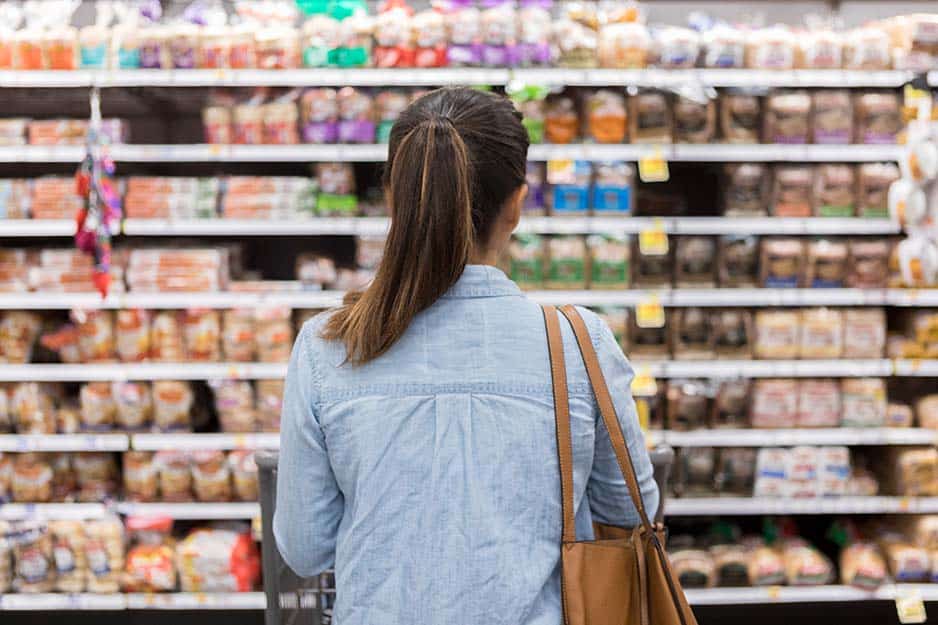 A woman scours the aisle for the best deal on a loaf of bread.