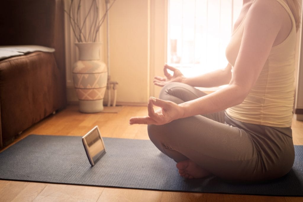 A woman sitting in meditation while being guided by an app on her phone