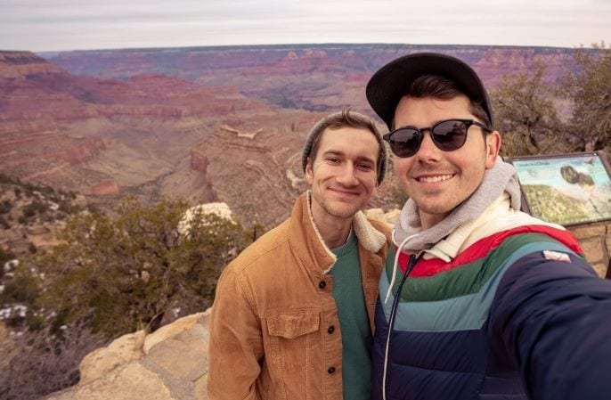 A young couple stops to take a selfie on a trail during their cross country move. They are both smiling. 