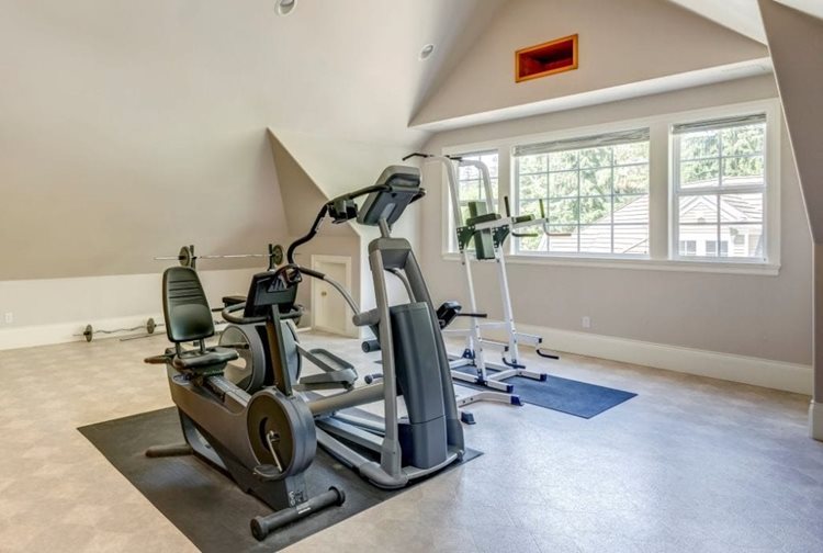 An attic space has been converted into a home gym. There are three large pieces of workout equipment placed atop rubber floor mats. 