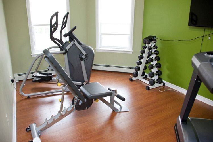 A small bonus room has been converted into a home gym. There are three large pieces of workout equipment and a dumbbell tree. 