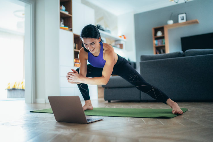 A woman is holding a yoga pose in her living room as she watches an online yoga instructor on her laptop.
