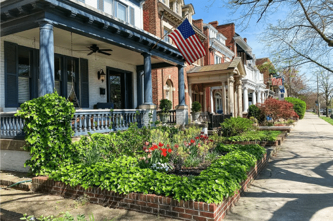 A row of charming homes in the Museum District of Richmond, Virginia, in the spring. Flowering plants are blooming in front of every door, and the sun is casting playful shadows on the sidewalks.