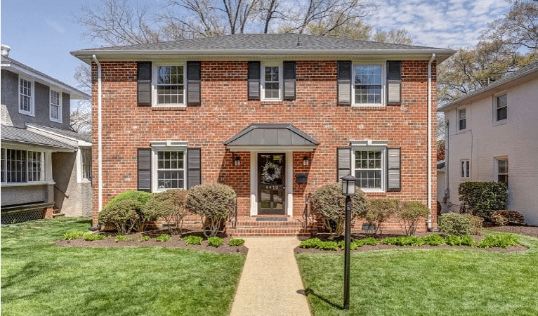 A brick, colonial-style home in the Colonial Place neighborhood of Richmond, Virginia. The home is two stories with red brick and black shutters. The yard is neatly kept, and there’s a retro light post beside the walkway.