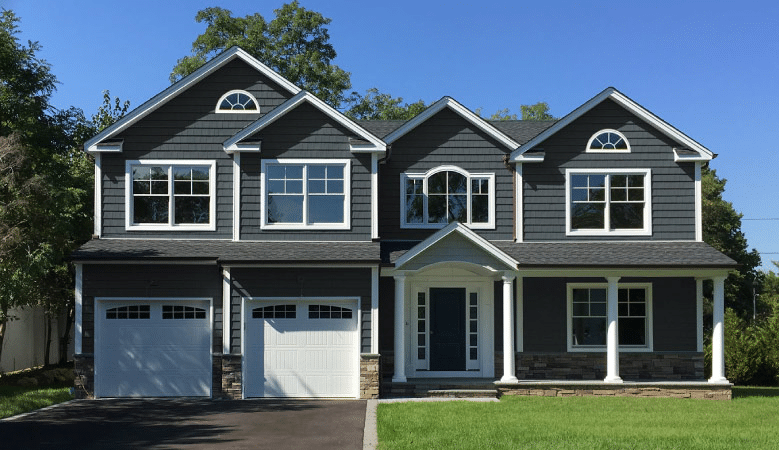 A new construction, two-story home in Plainview, New York, on Long Island. The blue siding home features several gables, stone veneer, two one-car garages, and a covered porch with columns.