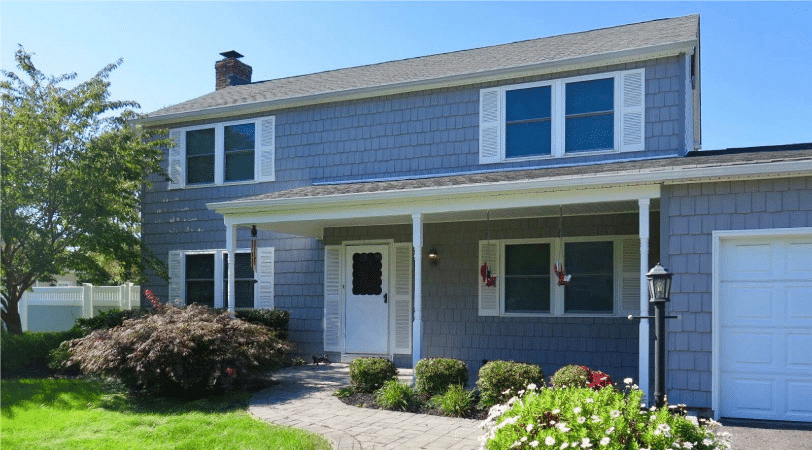 A two-story Colonial home in Stony Brook, New York. The home has shingles similar to a Cape Cod, painted a light blue.