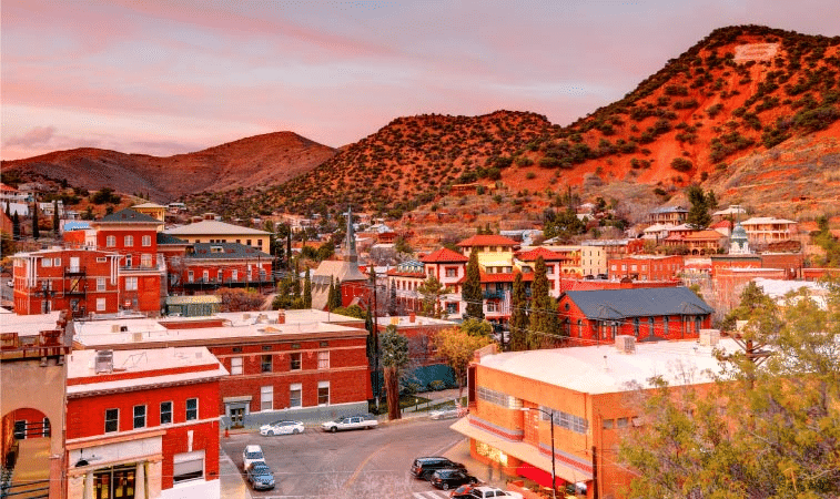 View of the town of Bisbee, Arizona, during sunset. Hills surround the town and many of the red-, yellow-, and orange-colored buildings are made more vibrant by the setting sun.