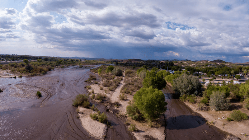 The Hassayampa River in Wickenburg, AZ, under a bright sky filled with fluffy clouds.