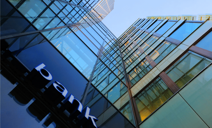 The view while looking up at a tall, glass-and-steel bank building. 