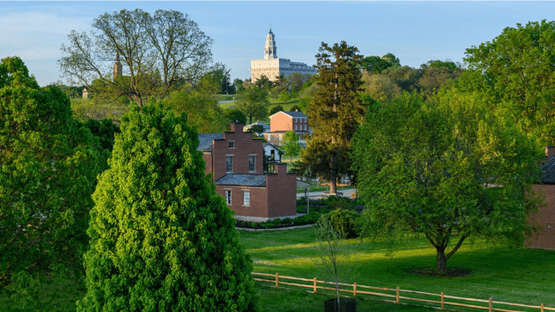 The town of Nauvoo, Illinois, with brick buildings, lush green lawns, mature trees, and the LDS Temple in the background.