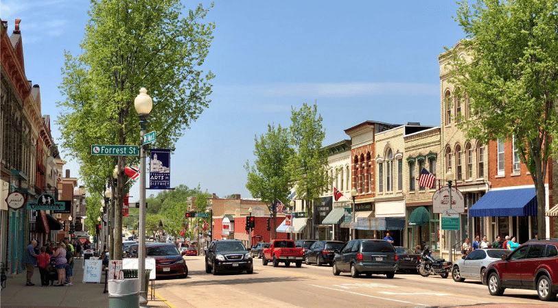 Locals walk and drive through downtown Stoughton, Wisconsin, on a sunny, summer day. 