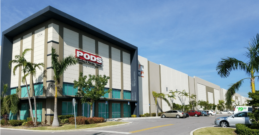 It’s a sunny day in Miami, Florida, at the PODS Storage Center. There are several palm trees planted outside the building and throughout the parking lot.