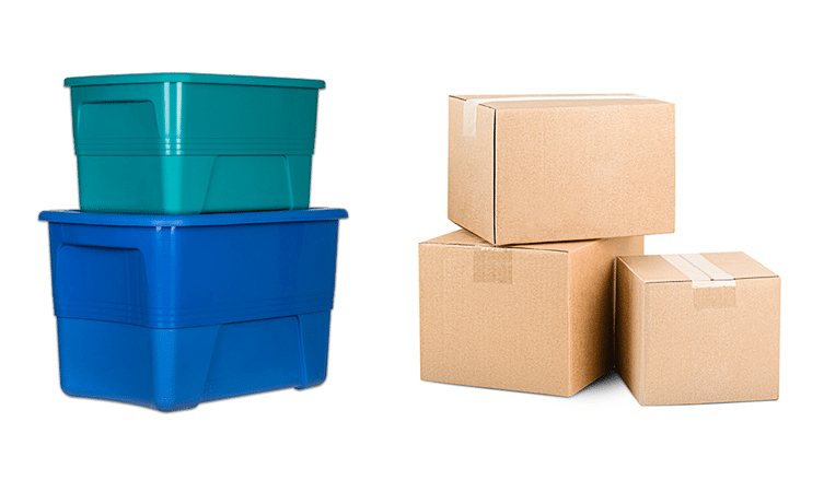 A medium green plastic storage bin stacked atop a larger blue bin, beside three cardboard boxes. 