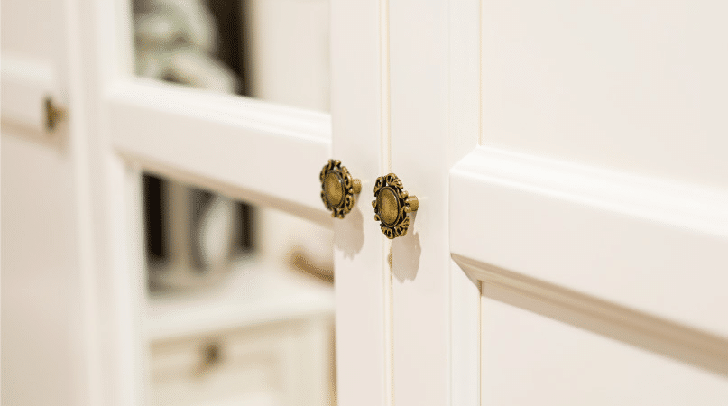 Close-up view of white cabinets with vintage-style bronze cabinet pulls in a modern farmhouse kitchen. One of the cabinet doors has a mirrored face and is reflecting another corner of the kitchen.