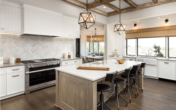 A modern farmhouse kitchen with various lighting elements: sconces, pendant lights, large windows to let in natural light, and under-cabinet lighting. 