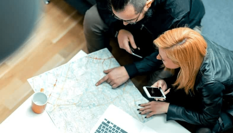 View from above of a couple looking over a map while planning their move in Texas. They have their mobile phones and a laptop nearby. 