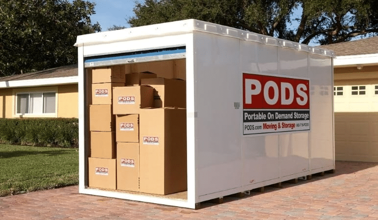 A PODS portable moving and storage container is almost fully loaded with moving boxes. The container is positioned in a residential driveway and its signature blue door is open.