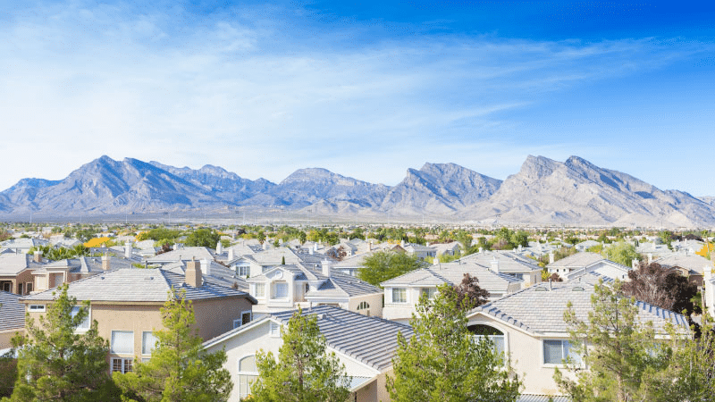 Treetop view of the Summerlin neighborhood in Las Vegas, Nevada. Rows of homes line the foreground, interspersed with trees, and there's a rocky mountain range in the distance.
