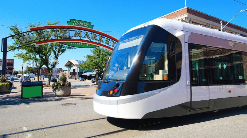 A KC Streetcar is waiting at a stop outside the Historic City Market in Kansas City, Missouri, on a sunny summer day.