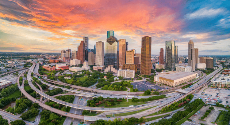 An aerial sunrise view of Houston — one of the best places to live in Texas — features half a dozen curving freeways wrapped around Downtown with lush greenery filling the gaps between them.