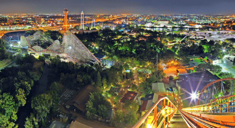 Nighttime view of Arlington, Texas, from the top of a roller coaster at Six Flags Over Texas. The city is illuminated with both residential and street lights and other roller coasters and tall city buildings can be seen in the distance.