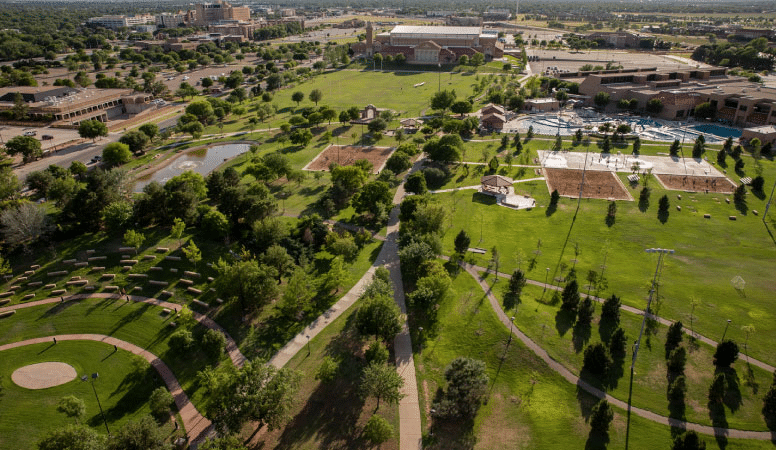 Aerial view of the Texas Tech University campus in Lubbock, Texas, with the city in the background. It’s late in the afternoon and the sun is bright, casting long shadows behind trees and buildings.