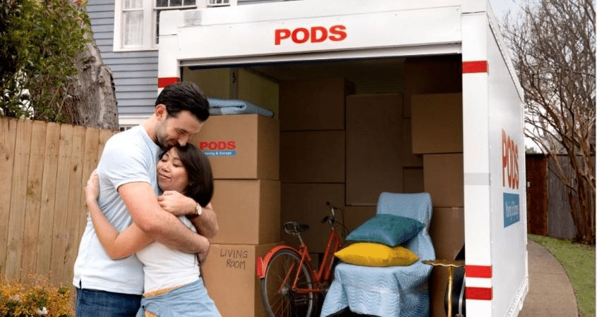 A couple is hugging in front of their PODS portable moving container, which they’ve just finished loading with boxes, furniture, and a bicycle for their move.