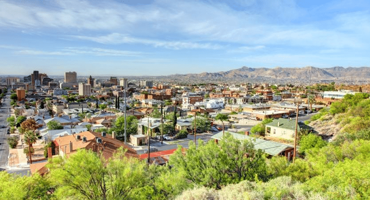 A sunny, tree-top view of El Paso — one of the best places to live in Texas — featuring residential buildings in the foreground, followed by taller city buildings, and a mountain range in the distance.