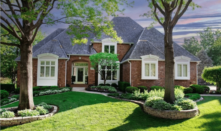 A 1.5 story, red brick house in Leawood, Kansas. The frames around the door and windows are painted white to contrast the rest of the home. Mature trees and perennial landscaping decorate the front yard.