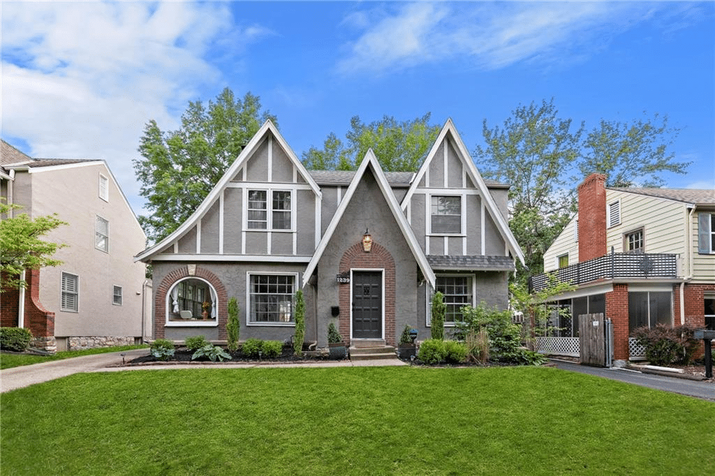 A charming Tudor house in the Waldo neighborhood of Kansas City, Missouri. The two-story home is painted gray with white and brick accents. The lawn is short and neat and there are a variety of plants in the front of the house.
