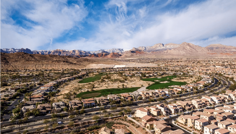 Aerial view of the Summerlin community in Las Vegas, Nevada. Rows upon rows of large residential homes line the streets and there are mountain ranges in the distance. 