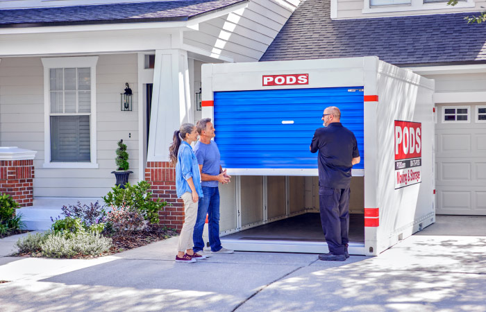 A mature couple is standing together in front of a PODS portable moving container as the PODS driver opens the container door. 