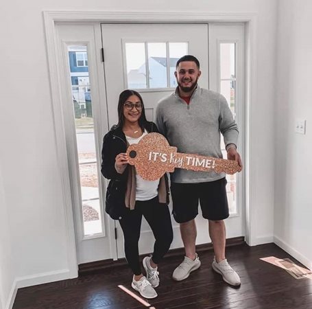 A happy expectant couple is holding a large paper key which represents the new home they just purchased. 