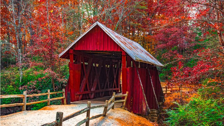 The historic red, wooden Campbell's Covered Bridge surrounded by autumnal foliage in Landrum, South Carolina.