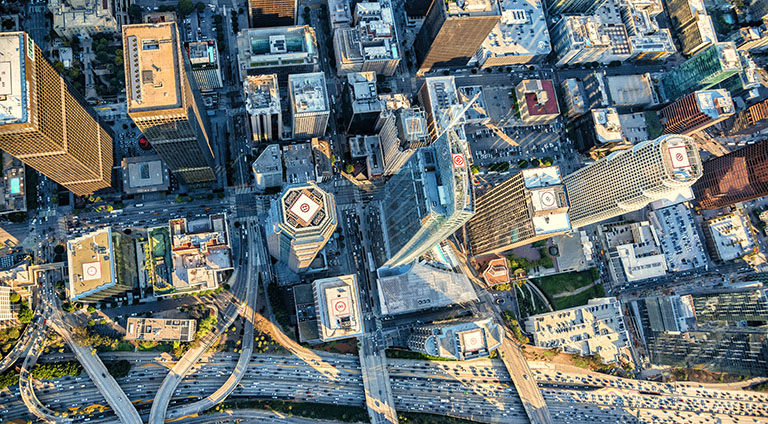 Aerial view looking straight down on downtown Los Angeles. Cars are driving up and down the freeways between large shadows cast by the city’s skyscrapers.