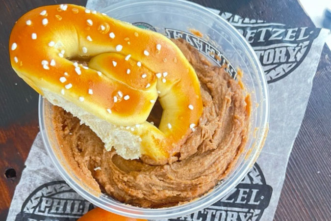 A soft and salty, figure-eight pretzel in a tub of tasty dip from Philly Pretzel Factory.