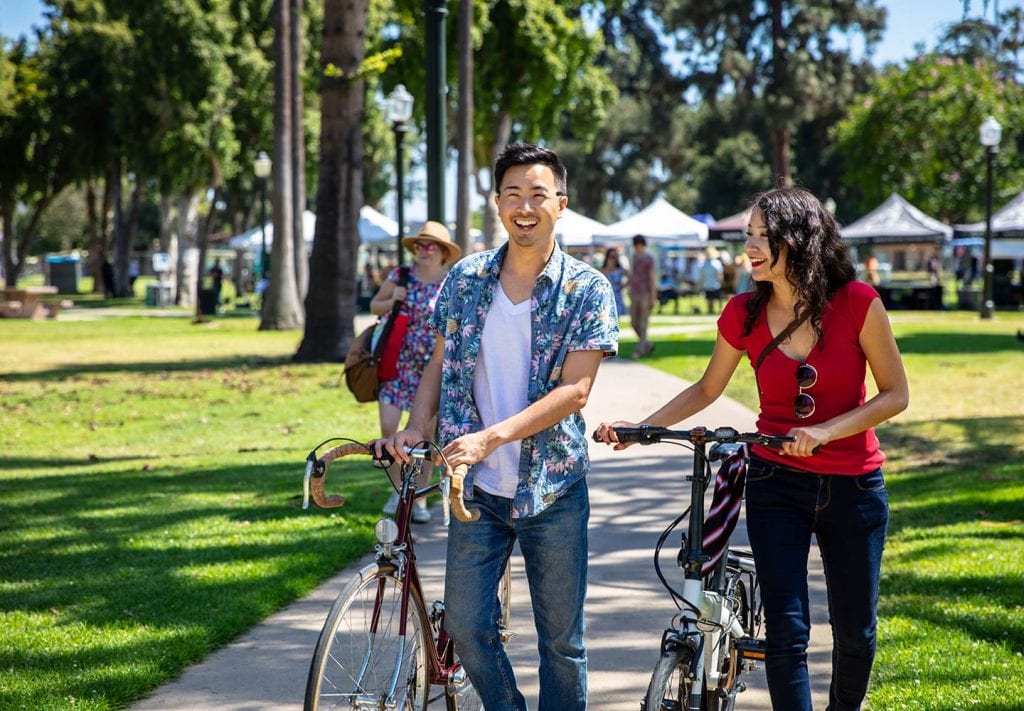 A couple is walking their bikes along a path outside a local market