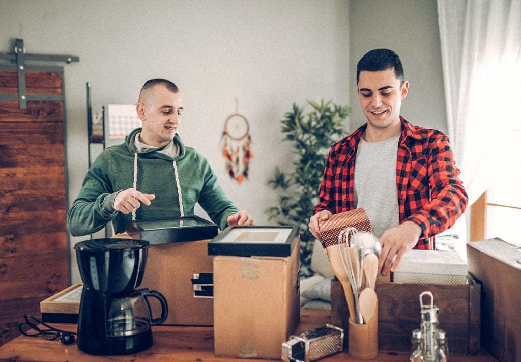 Two roommates are standing in front of moving boxes, unpacking their kitchen in their new Seattle apartment.