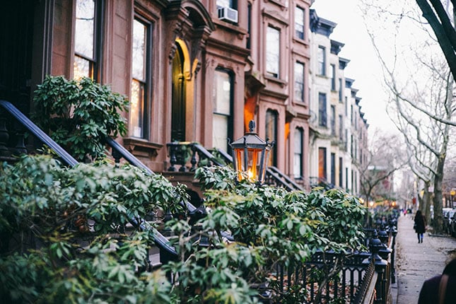An angled view of a row of townhouses in the Park Slope neighborhood of Brooklyn. The homes have a uniform look to them, all well-kept and with decorative plants around their front steps.