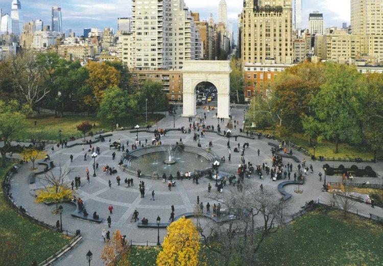 Aerial view of Washington Square Park in New York City’s Greenwich Village on an overcast day. Dozens of people are enjoying a cool autumn day around a popular fountain in the park.