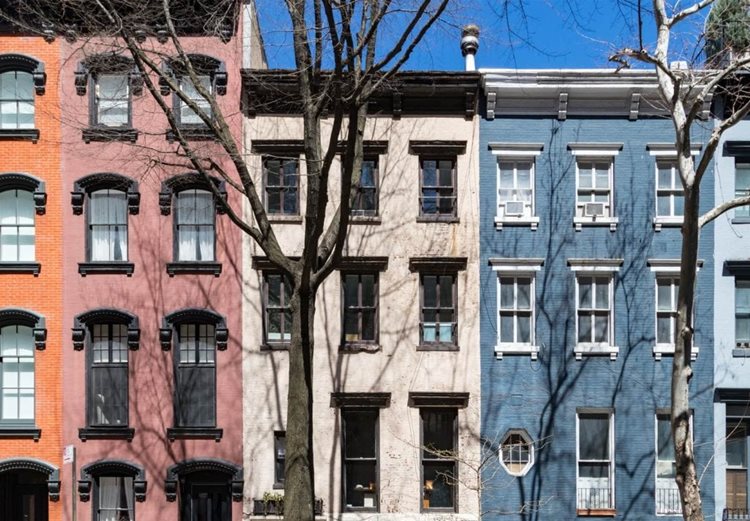 A row of apartment buildings in the Williamsburg neighborhood of The Bronx. The sides of the buildings are connected, and some of them share features, like height and window styles, but each is painted a unique color.